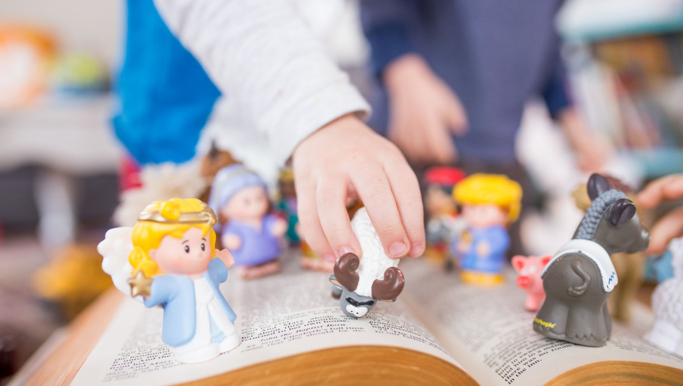 Child playing with Christmas figurines over an open bible